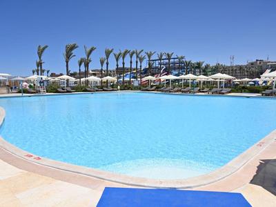 Duży basen na zewnątrz z czystą wodą, parasolami i palmami w tle pod słonecznym niebem.