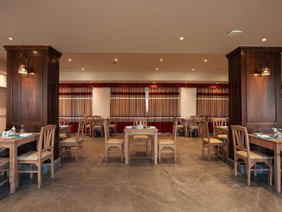 Spacious hotel restaurant with wooden chairs and tables under warm lighting.