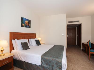 Modern furnished hotel room with double bed, nightstands, and seating area.