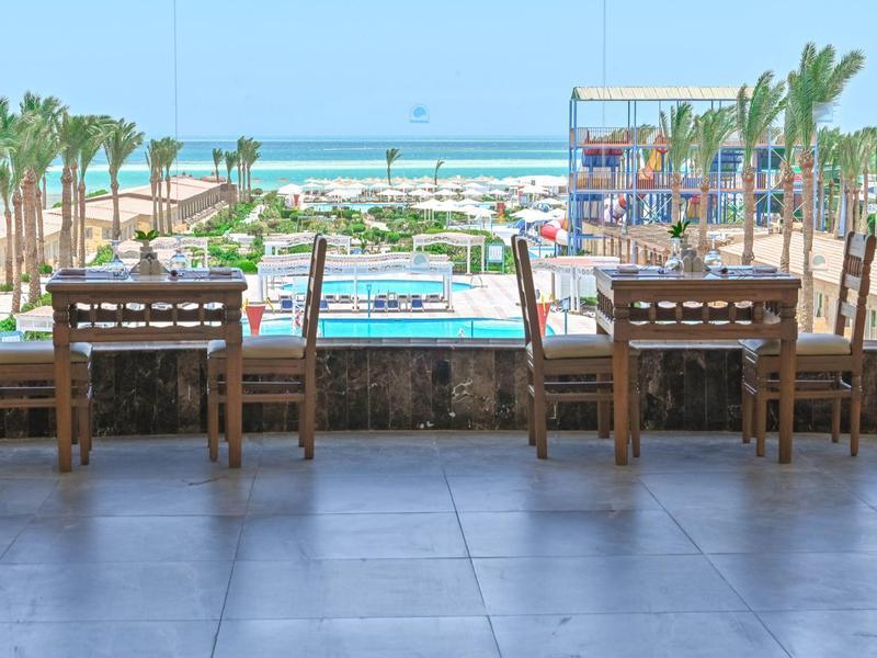 Vue sur une piscine avec des chaises longues, des palmiers et la mer en arrière-plan par une journée ensoleillée