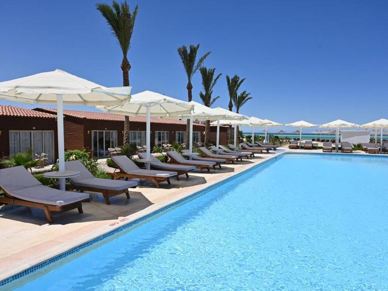 Grand piscine extérieure avec chaises longues et parasols sous un ciel bleu clair dans un hôtel