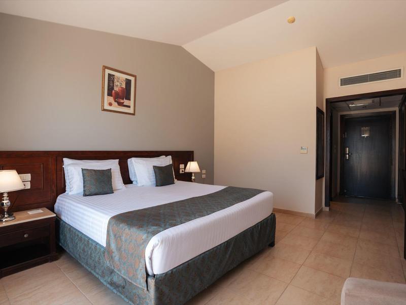 Chambre d'hôtel lumineuse avec grand lit, tables de chevet et lampe près d'une porte ouverte.