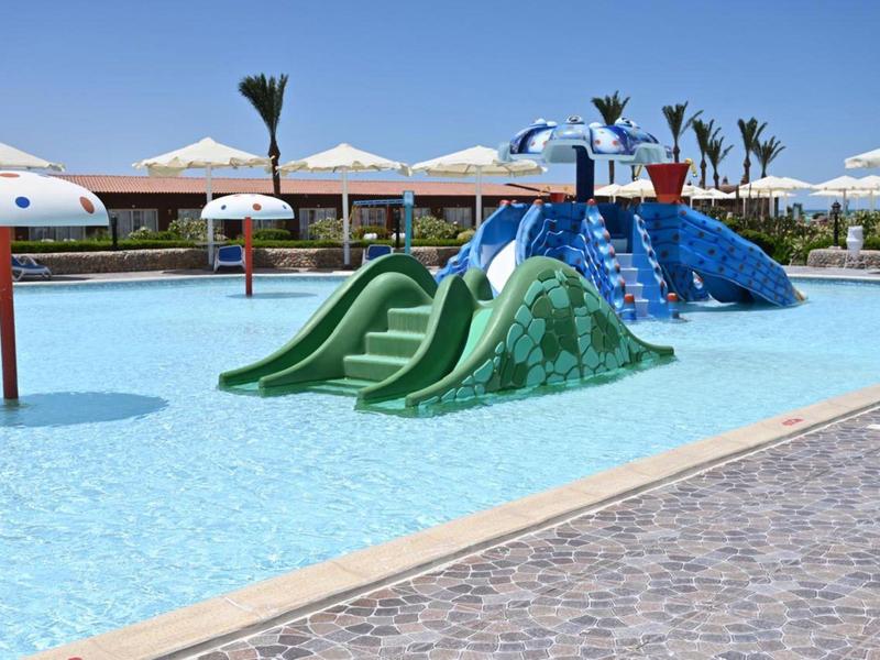 Espace de jeux pour enfants avec toboggans colorés et jeux d'eau dans une piscine peu profonde sous un ciel dégagé.