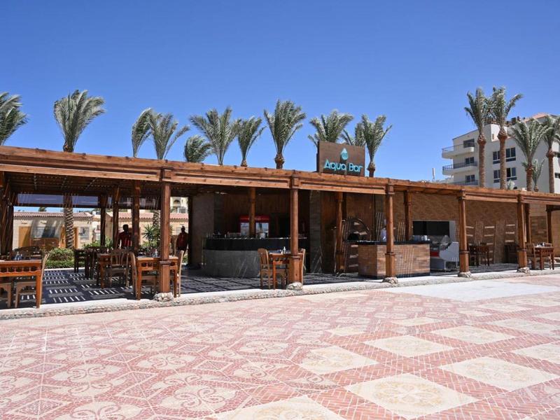 Padiglione aperto sulla spiaggia con struttura in legno, tavoli, sedie, palme sullo sfondo