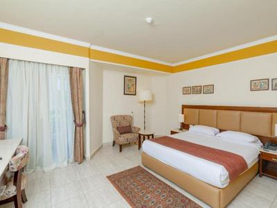 Chambre d'hôtel lumineuse avec lit double, bureau, fauteuil et vue sur le balcon.