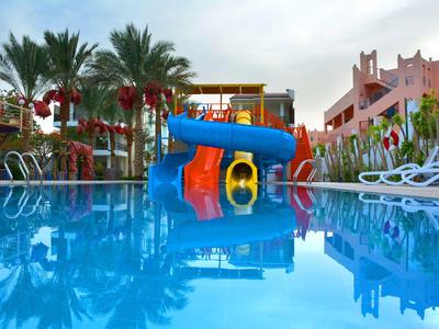Piscine d'hôtel avec toboggans aquatiques et chaises longues sous les palmiers.