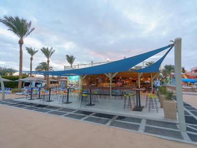 Espace bar extérieur moderne avec voile d'ombrage bleue et palmiers au crépuscule