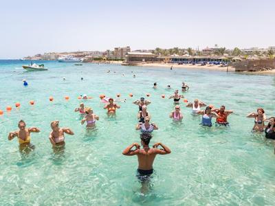 Des personnes font de l'aquagym dans une mer claire près d'un hôtel en bord de mer.