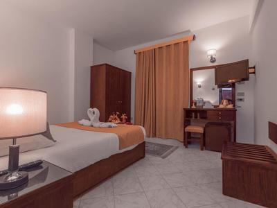 Chambre d'hôtel bien éclairée avec lit simple, bureau et rideaux aux tons chauds.