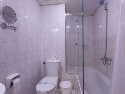 Petite salle de bain d'hôtel avec toilettes, douche en verre et baignoire dans un intérieur carrelé clair