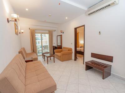 Salon lumineux avec canapés beiges, sol carrelé et accès à un balcon dans une chambre d'hôtel.