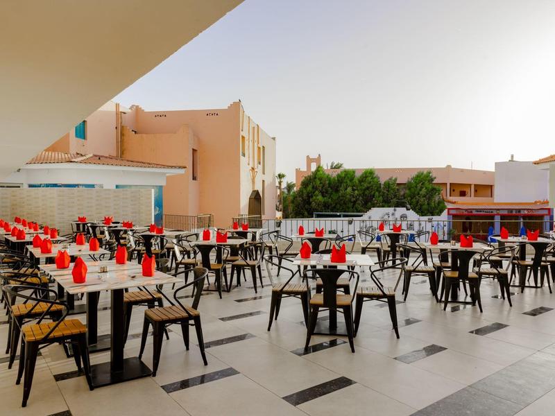 Grande terrasse avec plusieurs tables, chaises et verres décorés en rouge dans un espace extérieur d'hôtel