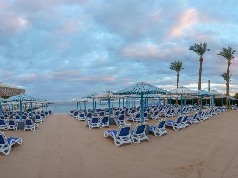 Grande zone de piscine avec des chaises longues bleues et des parasols sous un ciel nuageux
