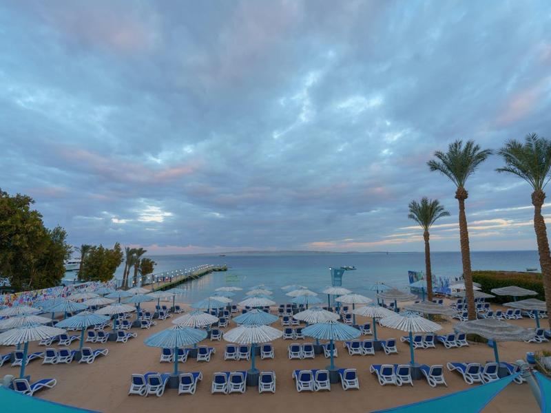 Vue sur une plage avec des chaises longues et des parasols sous un ciel nuageux et des palmiers au bord de la mer
