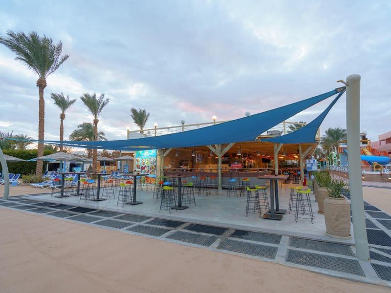 Espace bar extérieur moderne avec voile d'ombrage bleue et palmiers au crépuscule