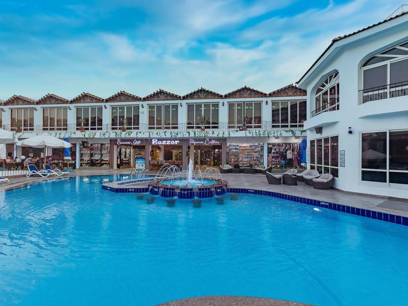 Grand piscine d'hôtel avec chaises longues autour et bâtiment à deux étages sous un ciel nuageux.