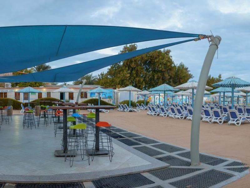 Espace ouvert avec tables, chaises et ombrage à côté d'une piscine avec transats.