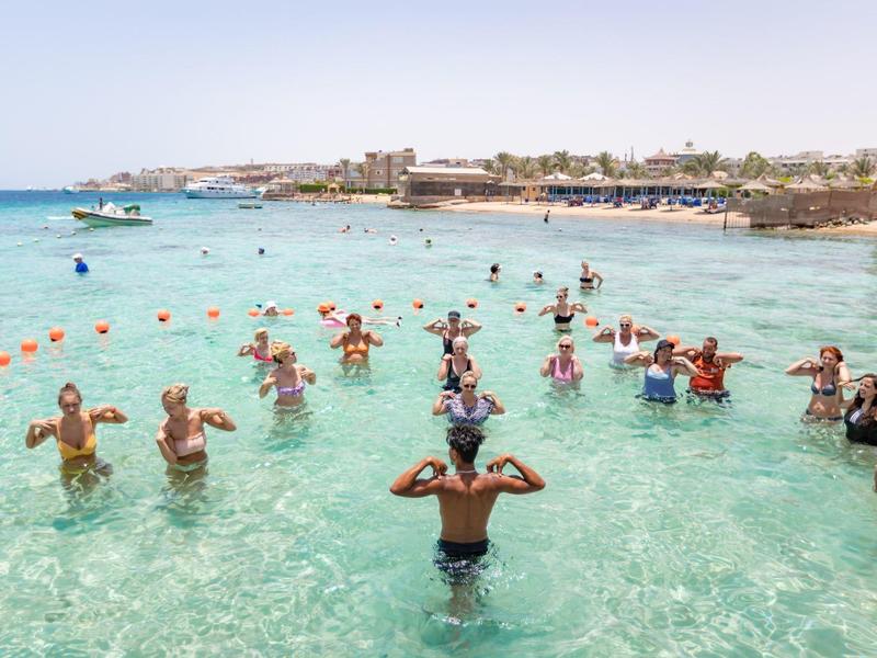 Groupe de personnes faisant de l'aquagym dans la mer claire près d'un hôtel en bord de mer.