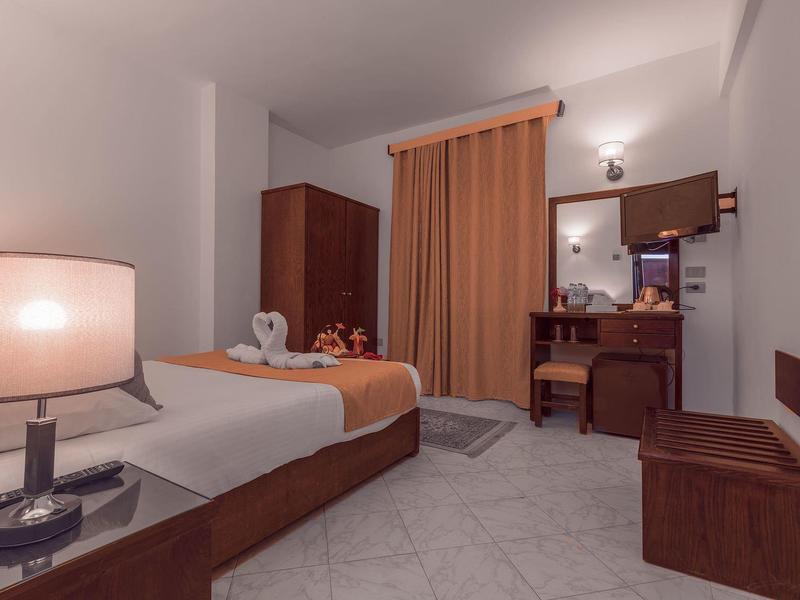 Chambre d'hôtel bien éclairée avec lit simple, bureau et rideaux aux tons chauds.