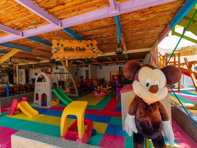 Espace de jeux intérieur coloré avec des équipements de jeu et une grande peluche dans une structure en bois.