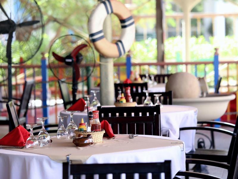 Table élégamment dressée avec nappes blanches et serviettes rouges dans un restaurant en plein air.