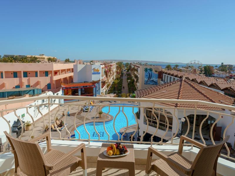 Balcon avec chaises et table avec fruits, vue sur piscine et bâtiments sous ciel dégagé