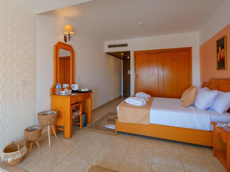 Chambre d'hôtel lumineuse avec lit double, meubles en bois et miroir près de la porte.