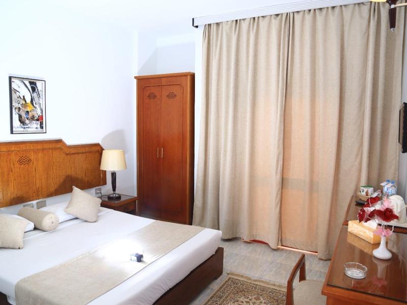 Chambre d'hôtel lumineuse avec lit double, meubles en bois et rideaux devant la fenêtre