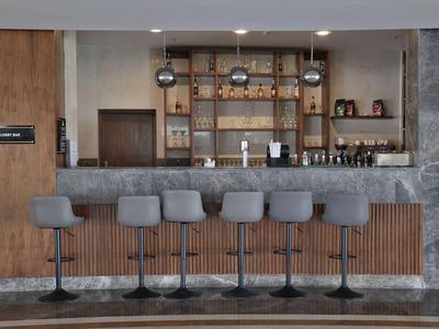 Moderní hotelový bar s šesti šedými barovými stoličkami a dřevěnými policemi v pozadí.