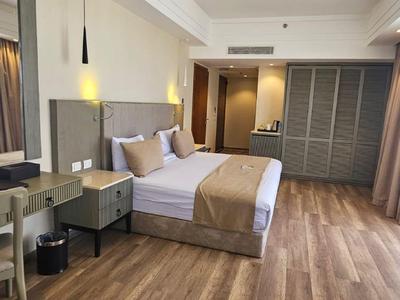 Modern hotel room with large bed, nightstands, desk, and wooden floor.