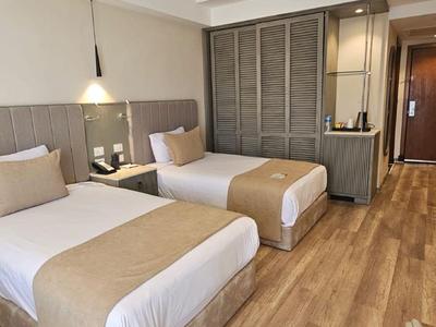 Modern hotel room with two single beds, wooden floor, and simple decor.
