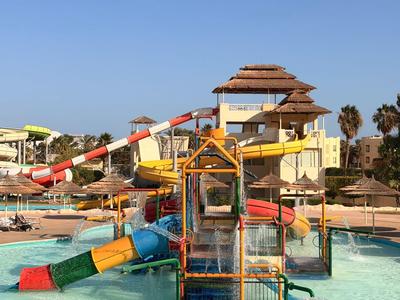 Water park with slides and umbrellas under clear sky next to a hotel.