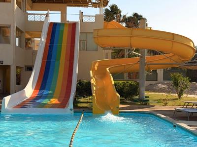 A pool with two water slides at a hotel resort under clear skies.