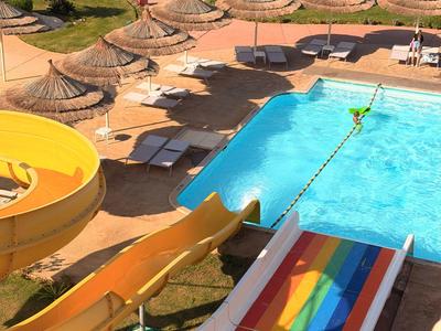 Colorful water slides area with pool and shaded umbrellas at a hotel resort.