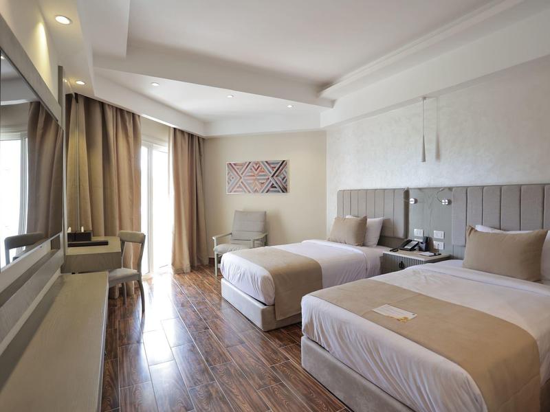 Chambre d'hôtel moderne avec deux lits simples, bureau et grande fenêtre avec rideaux.