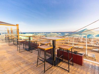 Terrazza all'aperto sul tetto con tavoli e sedie che si affacciano sul mare e sul cielo azzurro.