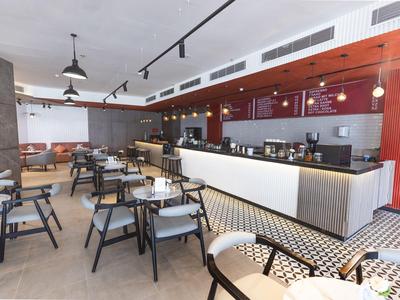 Sala colazione moderna con numerosi tavoli, sedie e un lungo bancone in un hotel.