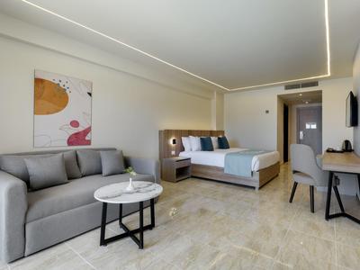 Camera d'hotel moderna con divano grigio, letto matrimoniale e scrivania in toni neutri.