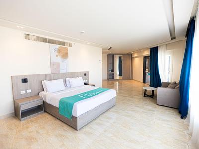 Camera d'hotel luminosa con letto matrimoniale, angolo salotto accogliente e grandi finestre con tende blu.