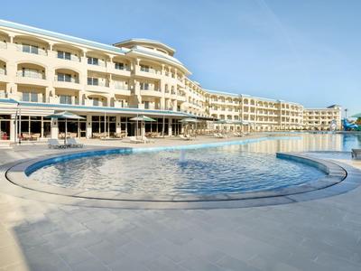 Grande edificio dell'hotel con più piani e piscina rotonda all'aperto in primo piano sotto un cielo sereno.