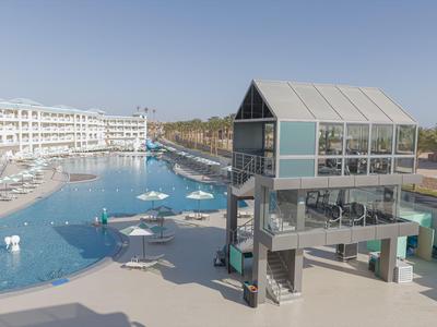 Area piscina moderna con ascensore in vetro e lettini in un resort alberghiero.