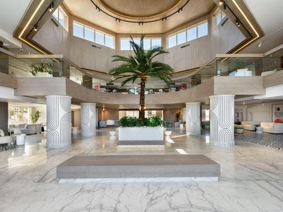 Ampia hall dell'hotel con palme, pavimento in marmo e arredi moderni sotto una cupola.
