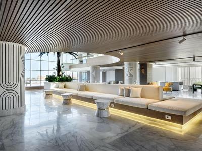 Area lounge moderna in hotel con sedute circolari e illuminazione indiretta sotto un soffitto in legno.