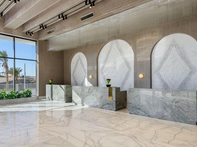 Area lobby moderna dell'hotel con banchi in marmo e grandi finestre con vista sulle palme.