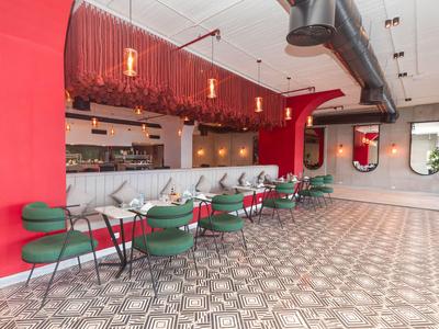 Ristorante moderno con pareti rosse, sedie verdi e pavimento piastrellato geometrico.