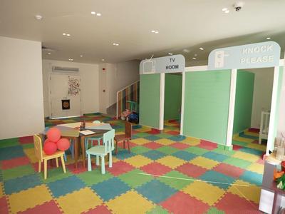 Area giochi per bambini colorata con tavoli, sedie e pouf in una stanza luminosa.