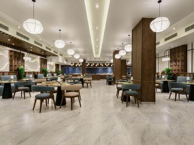 Area ristorante di un hotel arredata in modo moderno con tavoli, sedie e illuminazione decorativa.