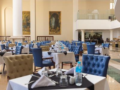 Elegantes Hotelrestaurant mit blauen und braunen Sesseln, gedeckten Tischen und Kunst an den Wänden.