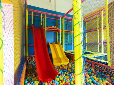 Buntes Indoor-Kinderspielplatz mit Rutschen und Ballpool, umgeben von Netzen.