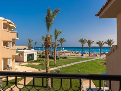Blick von einem Balkon auf einen Hotelgarten mit Palmen und dem Strand im Hintergrund.